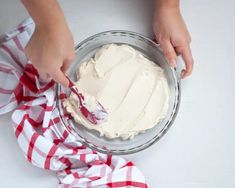 someone is spreading icing on top of a cake in a glass pie dish with a red and white checkered napkin