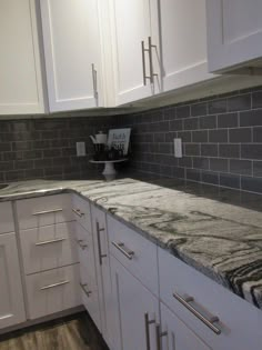 a kitchen with white cabinets and marble counter tops