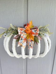 a wreath hanging on the side of a door with an orange and white bow attached to it