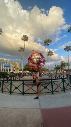 a woman standing in front of a sign with palm trees around her and clouds overhead