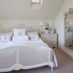 a white bed sitting inside of a bedroom next to a dresser and mirror on top of it