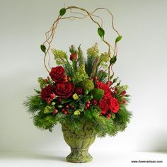 a green vase filled with red flowers and greenery on top of a white table