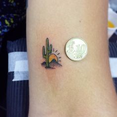 a small cactus tattoo on the right side of the arm, next to a one dollar coin