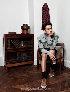 a young man sitting on top of a wooden chair in front of a book shelf