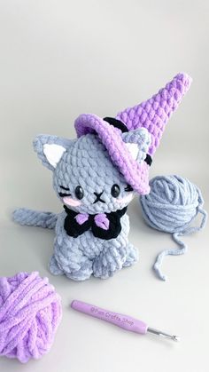 a crocheted cat sitting next to a ball of yarn and a knitting needle