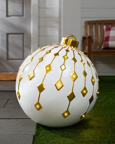 a large white ball with gold geometric designs on the top and sides, sitting on grass in front of a door