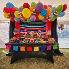 a table topped with lots of colorful balloons and desserts under a tented area