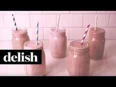 four mason jars with straws in them sitting on a counter next to a tiled wall