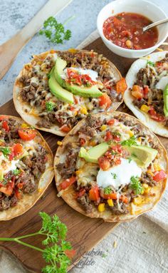 four tacos on a cutting board with salsa and avocado