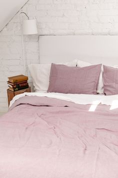 a bed with pink linens and pillows in a loft space next to a white brick wall