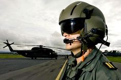 a man wearing a pilot's helmet and goggles standing in front of a helicopter