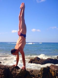 a man doing a handstand on top of rocks near the water's edge