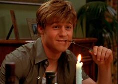 the young man is smiling while eating his food with a spoon in front of him