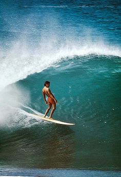 a man riding a surfboard on top of a wave in the ocean with blue water