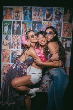 three women hugging each other in front of a wall with pictures on it