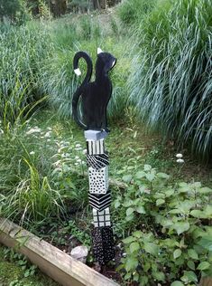 a black and white cat statue sitting on top of a lush green field next to tall grass