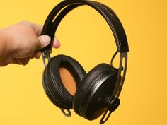 a pair of headphones being held by a person's hand on a yellow background