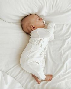 a baby laying on top of a white bed covered in blankets and pillows with his head resting on the pillow