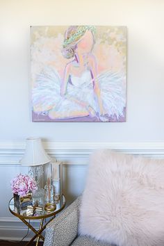 a painting hangs on the wall above a chair and side table with a lamp in front of it