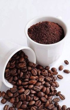 two cups filled with coffee beans on top of a white table next to each other