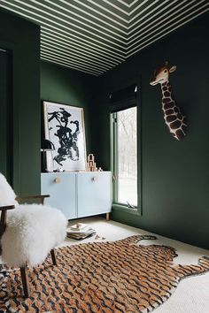 a giraffe head hanging on the wall next to a chair and rug in a green room