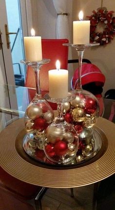 two wine glasses filled with ornaments on top of a glass table topped with candles and christmas balls