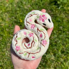 a hand holding two small white donuts with pink flowers on them in the grass