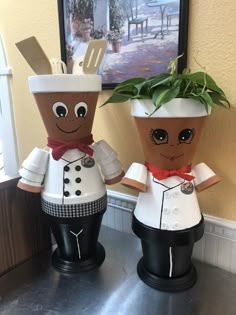 two paper mache people are standing next to each other on a counter top with a potted plant in the middle