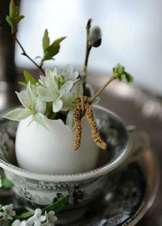 an egg with some flowers in it sitting on a saucer and silverware plate