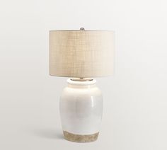 a white table lamp with a beige shade on the base and a gold trim around it