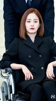 a woman sitting in a wheelchair next to a man wearing a black suit and tie