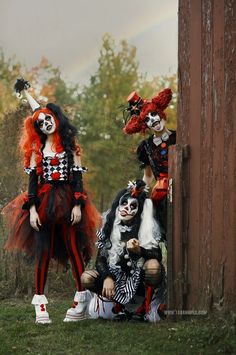 three clowns dressed up in costumes sitting on the ground next to a wooden fence