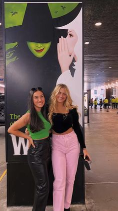 two women standing next to each other in front of a large sign with an advertisement on it