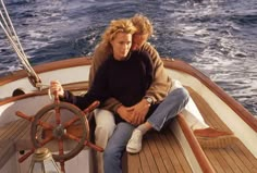 two people sitting on the deck of a boat with steering wheel in front of them