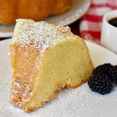 a piece of cake with powdered sugar and blackberries on a plate next to a cup of coffee