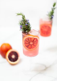 two grapefruit cocktails with rosemary garnish and blood orange slices on the side