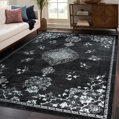 a black rug with white and blue flowers on it in front of a couch next to a window