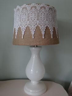 a white table lamp with a burlap shade on the bottom and lace trim around it