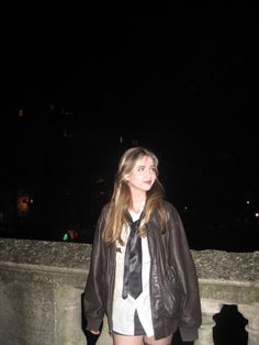 a woman in short shorts and a leather jacket is standing on a bridge at night