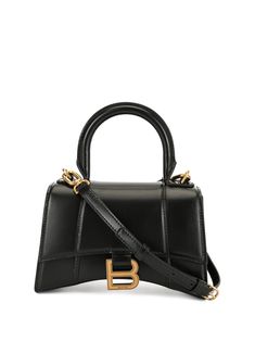 Hourglass XS top handle bag from BALENCIAGA featuring black, leather, gold-tone logo plaque, gold-tone hardware, single top handle, adjustable detachable shoulder strap, front flap closure, magnetic fastening, main compartment and internal logo patch.Width 7,48 in / 19 cm Height 5,12 in / 13 cm Depth 3,15 in / 8 cm Handle 3,54 in / 9 cm Strap 23,62 in / 60 cm Black Balenciaga, Balenciaga Women, Luxury Bag, Balenciaga Bag, Bottega Veneta Shoulder Bag, Black Leather Handbags, Handle Bag, Leather Handbag, Valentino Garavani