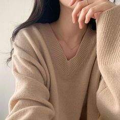 a woman wearing a tan sweater with her hand resting on her chin and looking at the camera