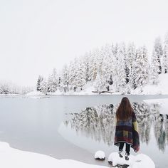 a woman standing on top of a snow covered shore next to a body of water