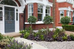 a house with many plants in front of it and two doors on the side of the house