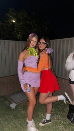 two women dressed up in costumes posing for the camera at a halloween costume party, one is wearing an orange and purple dress