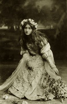 an old black and white photo of a woman wearing a dress with flowers in her hair