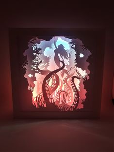 an illuminated shadow box with a silhouette of a mermaid and seahorse in the background