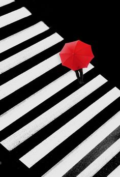 a person with an umbrella stands on the crosswalk in the dark and white stripes