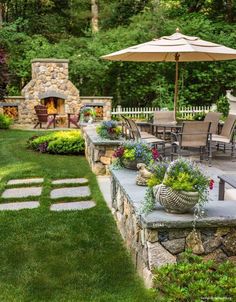 an outdoor patio with tables, chairs and umbrellas in the grass next to a stone fire place