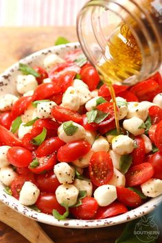 a bowl filled with tomatoes and mozzarella being drizzled with olive oil