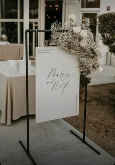 a sign that is on top of a stand in front of a table with flowers